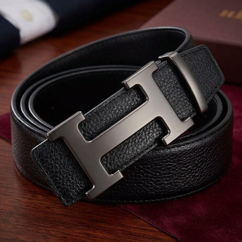 Men's black leather belt with gunmetal H buckle displayed on a wooden surface