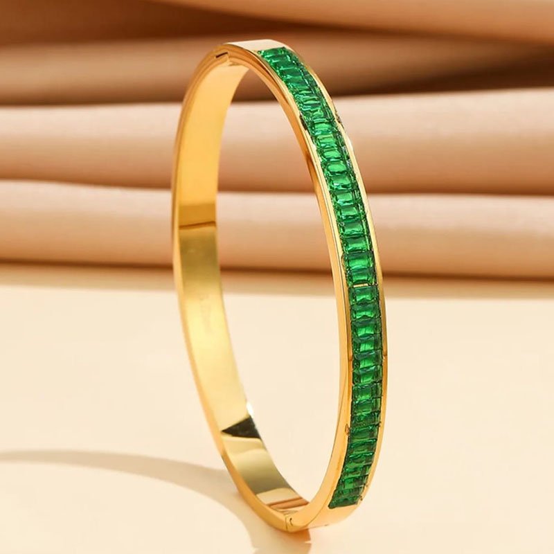 gold bracelet for women with green emerald crystals displayed on a neutral surface