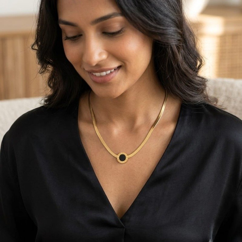 Gold black circle pendant necklace worn by woman with elegant design