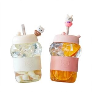 Cute glass cup with straw featuring bear and bunny designs held in hands